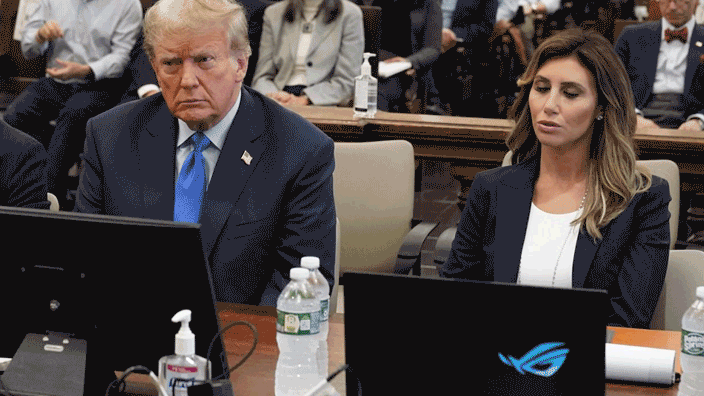 A photo of Donald Trump sitting next to his lawyer, who has an Asus gaming laptop. It's a still image, but we've edited it to make the laptop's RGB logo cycle through rainbow colours.